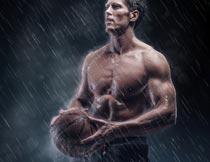 雨中雙手拿著籃球的肌肉男攝影圖片